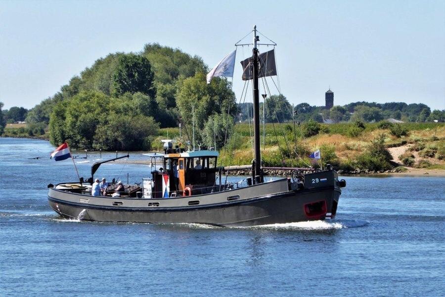 Rijksvaartuig RV 29 varend in open water, met groene oevers en de Nederlandse vlag zichtbaar.